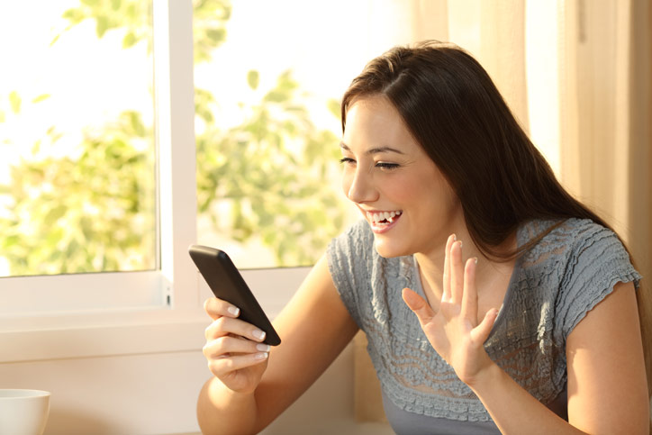 Eine junge Frau begrüsst ihre online Lehrperson auf dem Handy