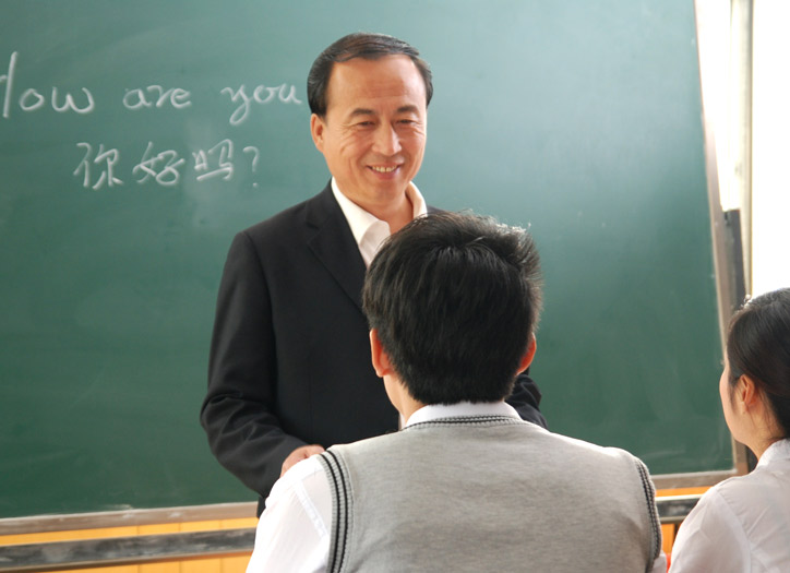A Chinese course in a small group. The teacher is standing in front of the students and is listening to them and smiling at them.