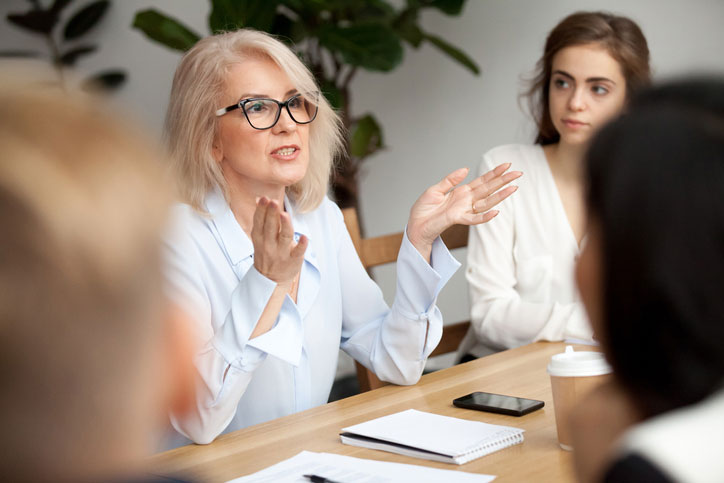 English course in a company. The teacher is speaking to the participants who are sitting around a table.