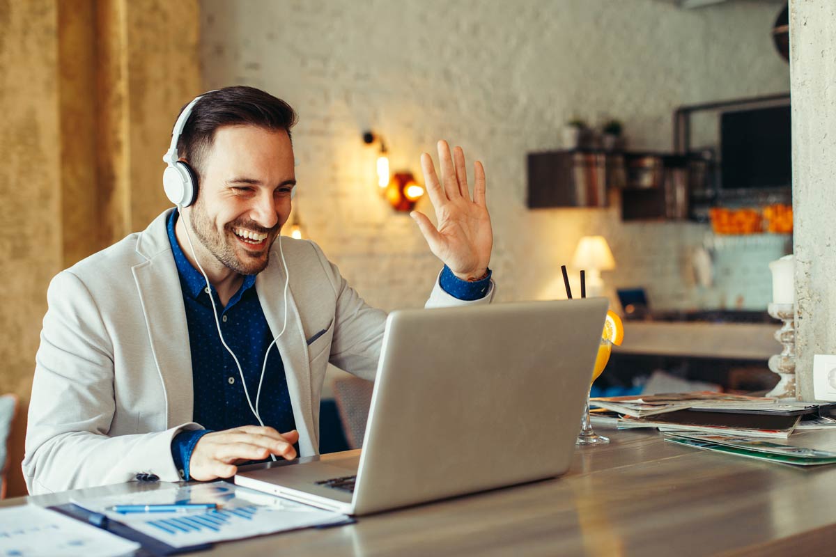 A man is learning English online via video conference an is waving at his teacher.