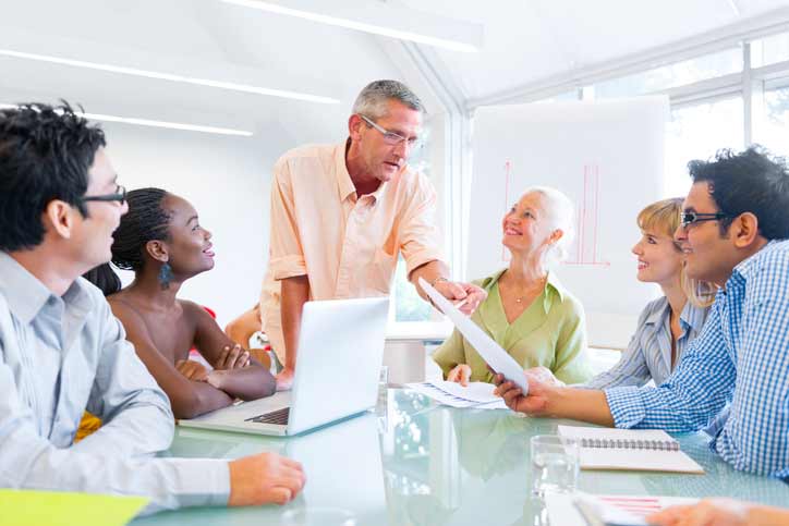 A French course in a company. The teacher is talking to the multi-ethnic employees, who are sitting around a table.