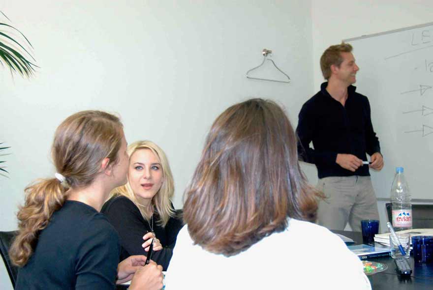 French language course in a small group at Sprachschule Schneider in Zurich. The French teacher is writing at the board.