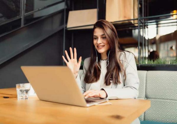 A young woman is learning German via video conference and is waving to her teacher.