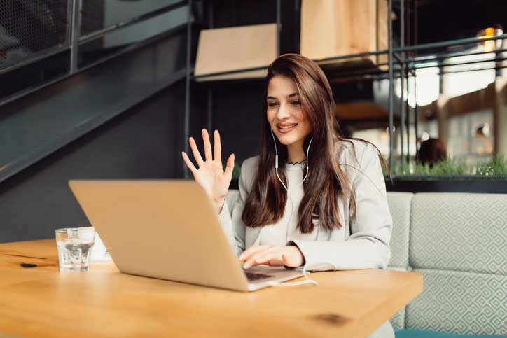 A young woman is learning German via video conference and is waving to her teacher.