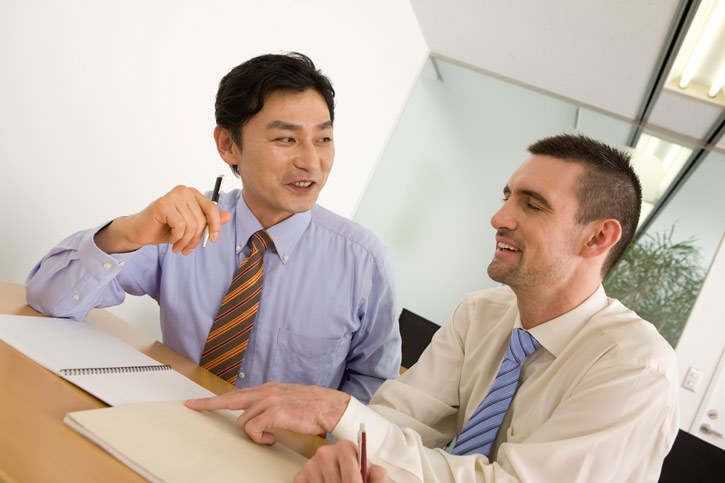 An employee is learning Japanese in a customised 121 language course in he's company and is sitting next to the teacher at the table.