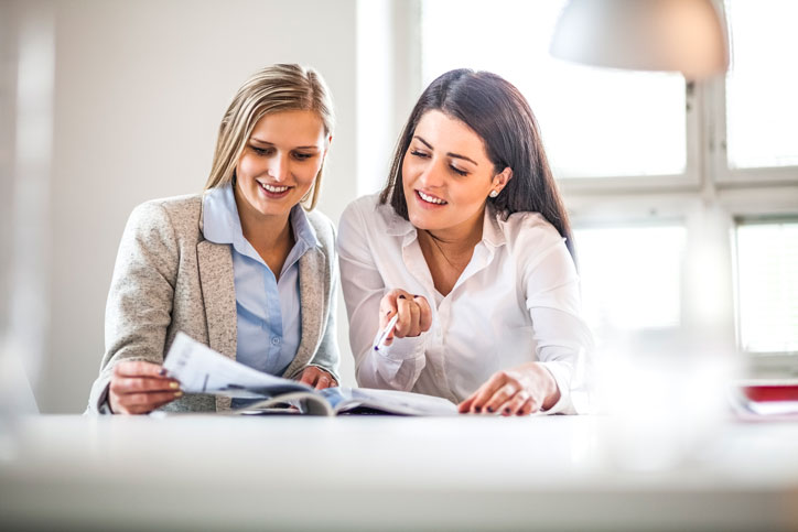 Businesswoman is learning Portuguese in a customised one-to-one course. Headteacher is sitting close to her pointing at a text